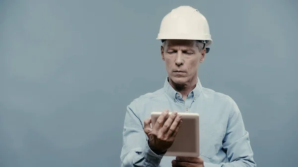 Engineer in hardhat using digital tablet isolated on grey — стоковое фото