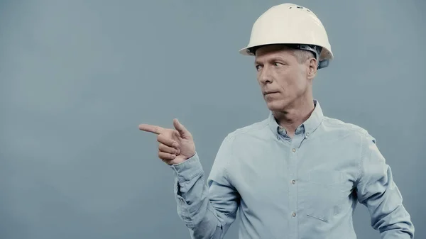 Middle aged businessman in hardhat pointing with finger isolated on grey — стоковое фото