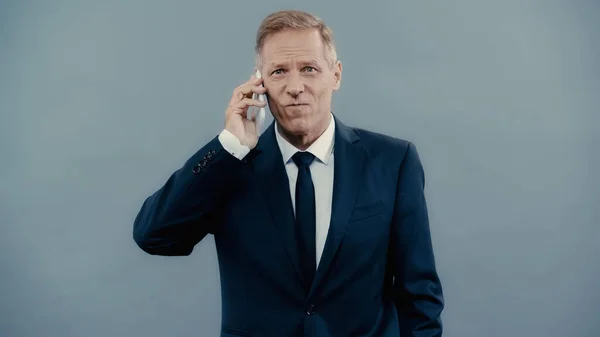 Displeased businessman in formal wear talking on cellphone isolated on grey — Stock Photo