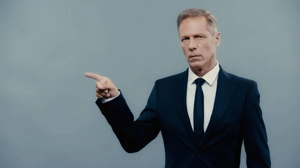 Mature businessman in formal wear pointing with finger isolated on grey — Stock Photo
