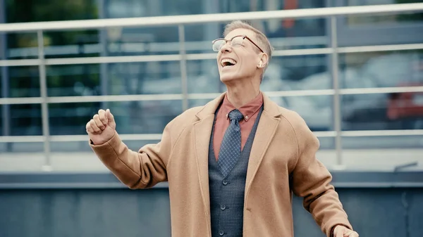 Excited businessman in coat and earphone singing on urban street — Stockfoto