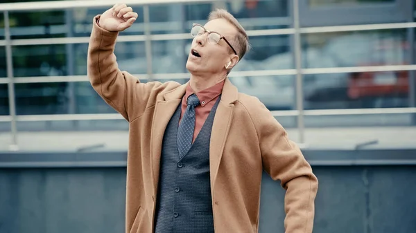 Mature manager in coat and earphone singing outdoors — Stock Photo