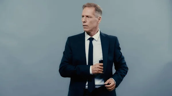 Mature businessman taking drinking flask from jacket isolated on grey — Stock Photo