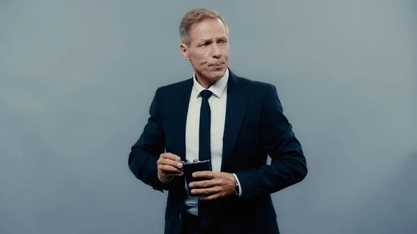 Бізнесмен тримає питну колбу і дивиться ізольовано на сірий — стокове фото
