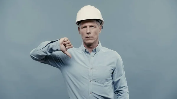 Middle aged engineer in hardhat showing dislike sign isolated on grey — Foto stock