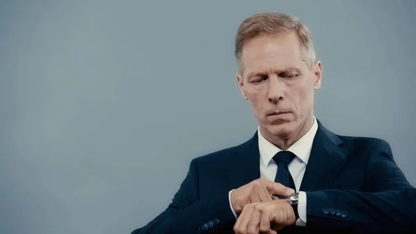 Homme d'affaires mature pointant vers la montre-bracelet isolé sur gris — Photo de stock