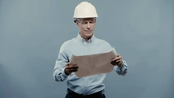 Smiling engineer in hardhat looking at blueprint isolated on grey — Photo de stock