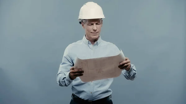 Ingénieur souriant en hardhat regardant le plan isolé sur gris — Photo de stock