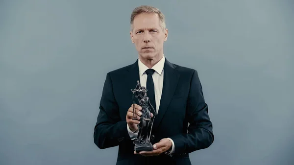 Lawyer holding statuette of femida and looking at camera isolated on grey — стоковое фото