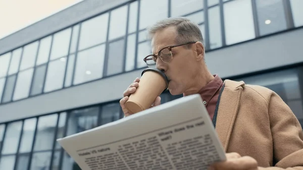 Maduro hombre de negocios bebiendo café y leyendo el periódico al aire libre - foto de stock