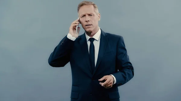 Stressed businessman talking on cellphone isolated on grey — Stock Photo