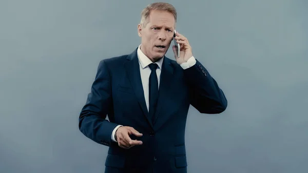 Hombre de negocios preocupado hablando en smartphone aislado en gris — Stock Photo