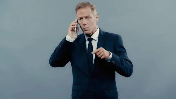 Homme d'affaires en colère parlant sur smartphone et pointant du doigt isolé sur gris — Photo de stock
