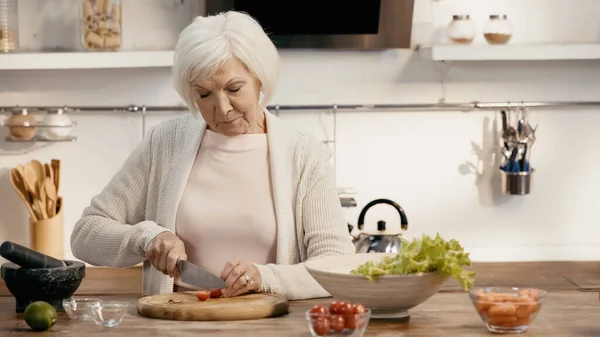 Mujer mayor cortar tomates cherry mientras se prepara la cena de acción de gracias - foto de stock