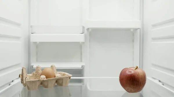 Red apple and egg in egg tray on shelf in refrigerator — Stock Photo