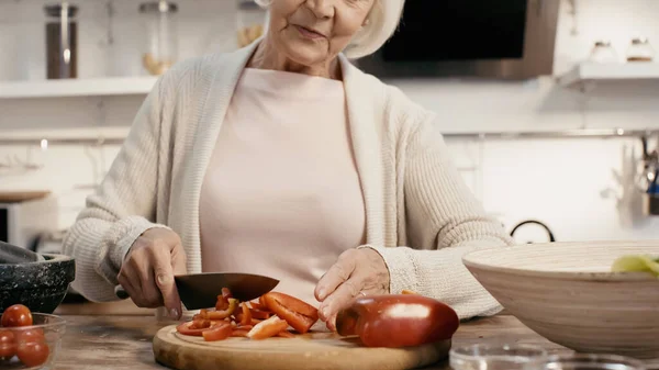 Vue recadrée de femme âgée coupant poivron sur planche à découper dans la cuisine — Photo de stock