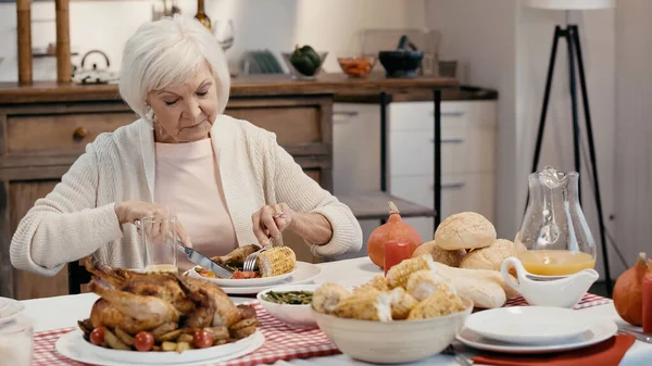 Pensionista mujer teniendo cena de acción de gracias cerca de pavo tradicional y maíz a la parrilla en la mesa - foto de stock