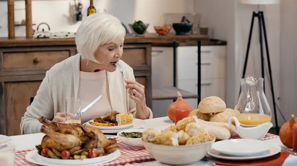 Femme âgée ayant dîner d'Action de grâces près de dinde rôtie, maïs grillé, jus d'orange et petits pains — Photo de stock