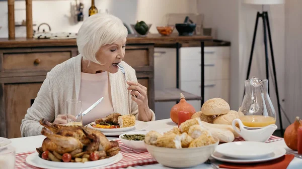 Anciana teniendo cena de acción de gracias cerca de pavo asado, maíz a la parrilla, jugo de naranja y bollos - foto de stock