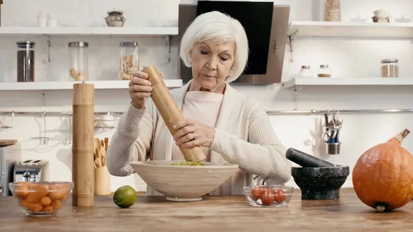 Senior woman seasoning vegetable salad while preparing thanksgiving dinner — стоковое фото