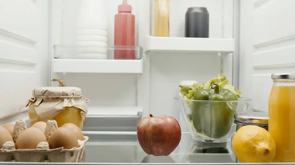 Fruits et légumes frais près des œufs, jus d'orange et bouteilles avec sauces au réfrigérateur — Photo de stock