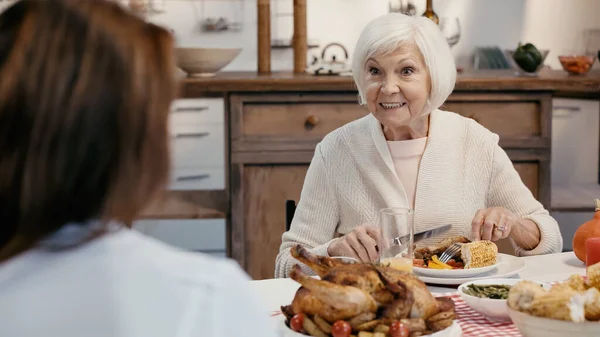 Senior woman smiling during thanksgiving dinner with blurred guest — Fotografia de Stock