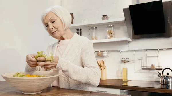 Elderly woman adding fresh lettuce to sliced bell pepper while preparing salad for thanksgiving dinner — Stock Photo