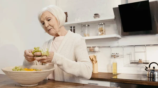 Elderly woman adding fresh lettuce to sliced bell pepper while preparing salad for thanksgiving dinner — Stockfoto