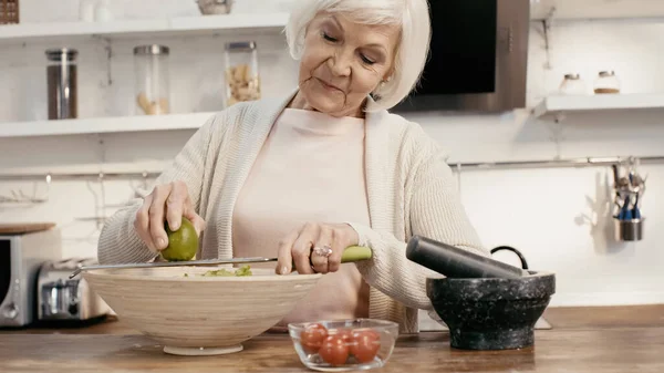 Elderly woman grating lime to vegetable salad for thanksgiving dinner — стоковое фото