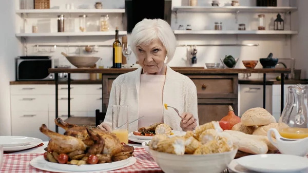 Displeased woman holding knife and fork during thanksgiving dinner in kitchen — Stockfoto