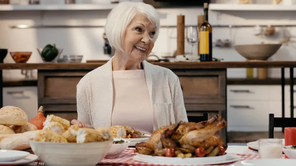 Feliz anciana sonriendo cerca de la cena de acción de gracias servida en la cocina - foto de stock