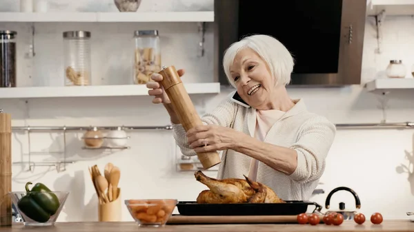 Mujer feliz sazonador pavo asado mientras habla en el teléfono inteligente - foto de stock