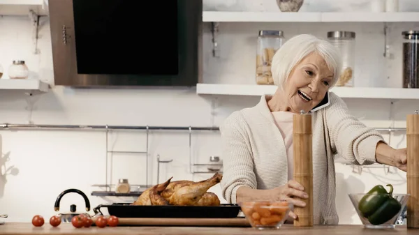 Happy senior woman talking on mobile phone near delicious turkey, spice mills and fresh vegetables — Stock Photo