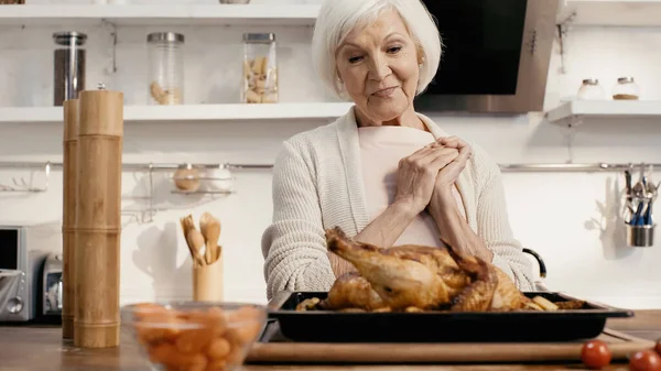 Pleased senior woman looking at delicious turkey near spice mills in kitchen — стоковое фото