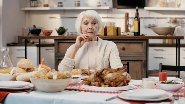 Thoughtful senior woman sitting alone at table served with thanksgiving dinner in kitchen — Fotografia de Stock