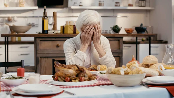 Depressed woman obscuring face with hands while sitting at table served with thanksgiving dinner — Stock Photo