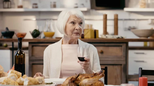 Happy senior woman holding glass of red wine during thanksgiving dinner — Stockfoto