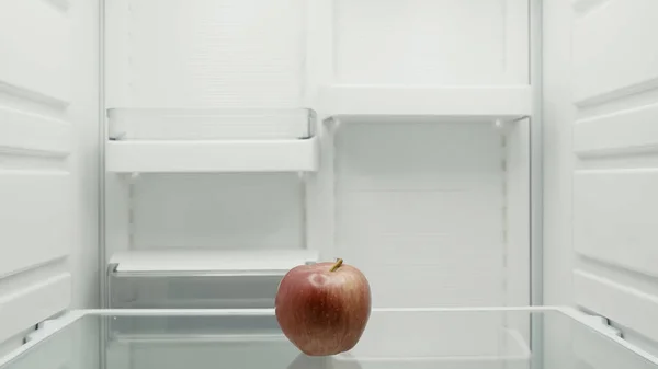 Ripe red apple on shelf in empty fridge — Stock Photo