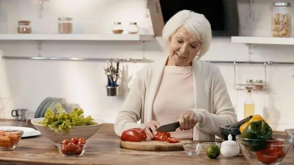 Mujer mayor sonriente cortar pimiento mientras se prepara la cena de acción de gracias - foto de stock