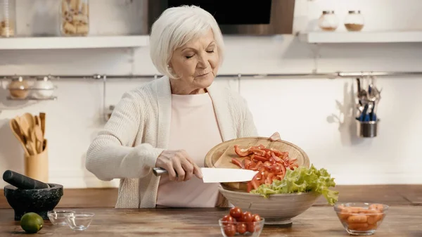 Elderly woman adding sliced bell pepper to vegetable salad for thanksgiving dinner — Photo de stock