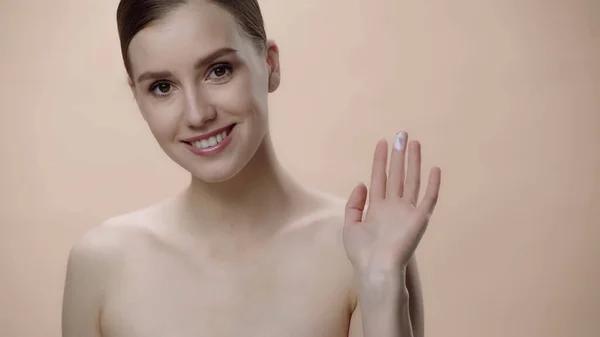 Happy young woman with bare shoulders showing fingers with face cream isolated on beige — Photo de stock