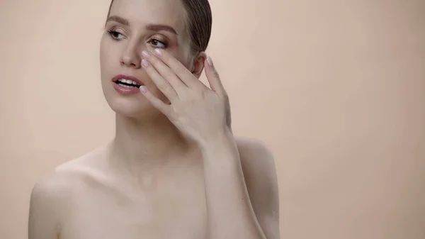 Young woman with bare shoulders and open mouth applying face cream isolated on beige — Stock Photo