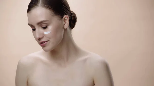Young woman with bare shoulders and cream on face isolated on beige — Stock Photo