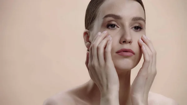 Young woman with bare shoulders applying cream on face isolated on beige — Foto stock