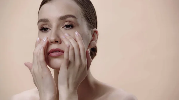 Woman with bare shoulders applying cream on face isolated on beige — Foto stock