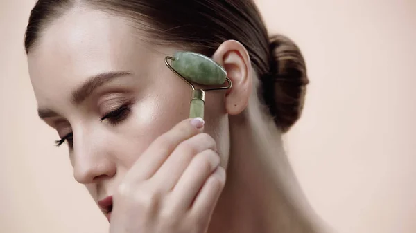 Young woman using jade roller isolated on beige — Stock Photo