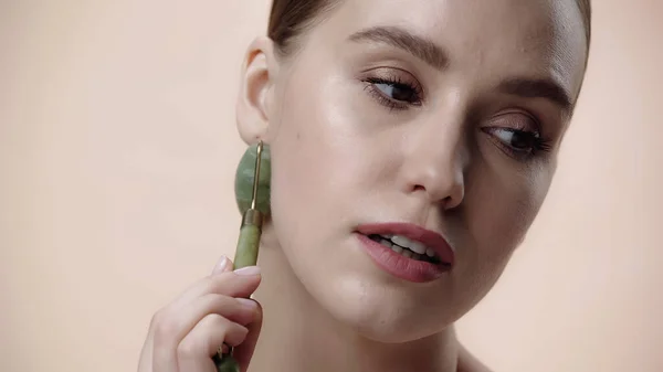 Pretty young woman using jade roller isolated on beige — Photo de stock