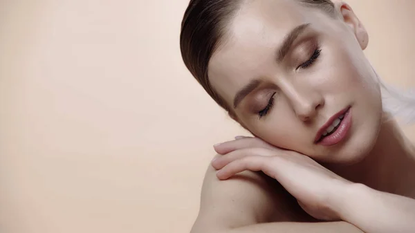 Feather near cheek of young woman with closed eyes isolated on beige — Stock Photo