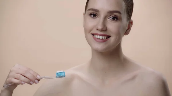 Smiling woman with bare shoulders holding toothbrush with toothpaste isolated on beige — Fotografia de Stock