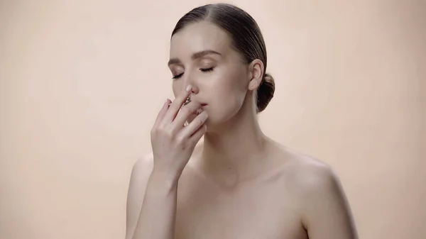 Young woman with bare shoulders smelling luxurious perfume isolated on beige — стоковое фото